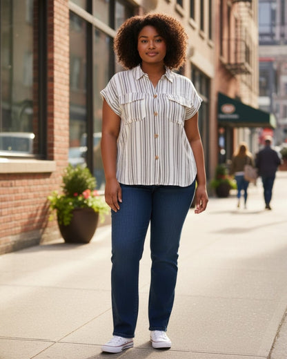 Woman in a striped shirt and blue jeans standing on a city sidewalk.