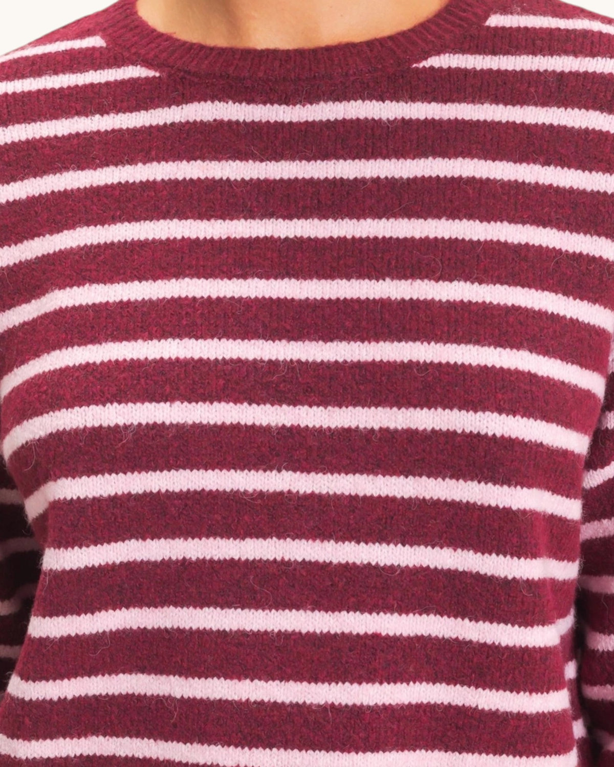 A close-up of a crewneck knit sweater with horizontal stripes in burgundy and light pink.