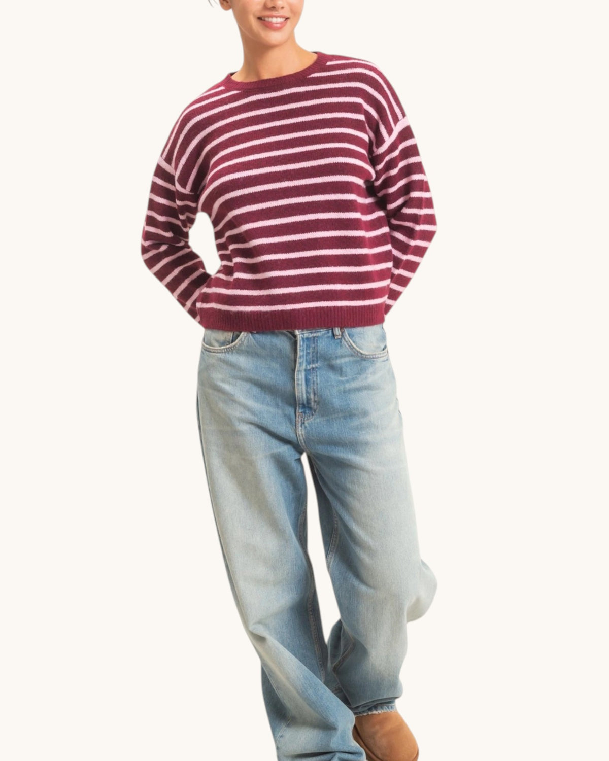 A woman wearing a burgundy and white horizontally striped knit sweater with light-wash blue jeans, shown from the mouth down against a plain off-white background.