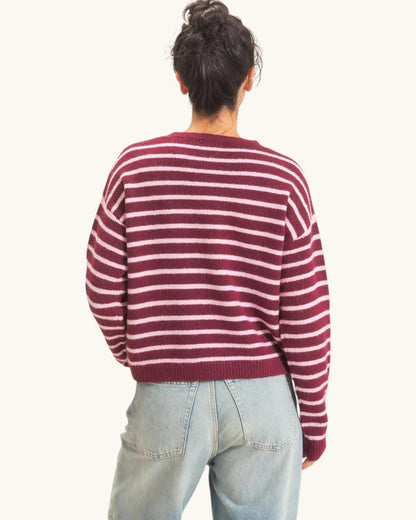 A person shown from the back wearing a burgundy and light pink horizontally striped knit sweater and light blue jeans against a plain off-white studio background.