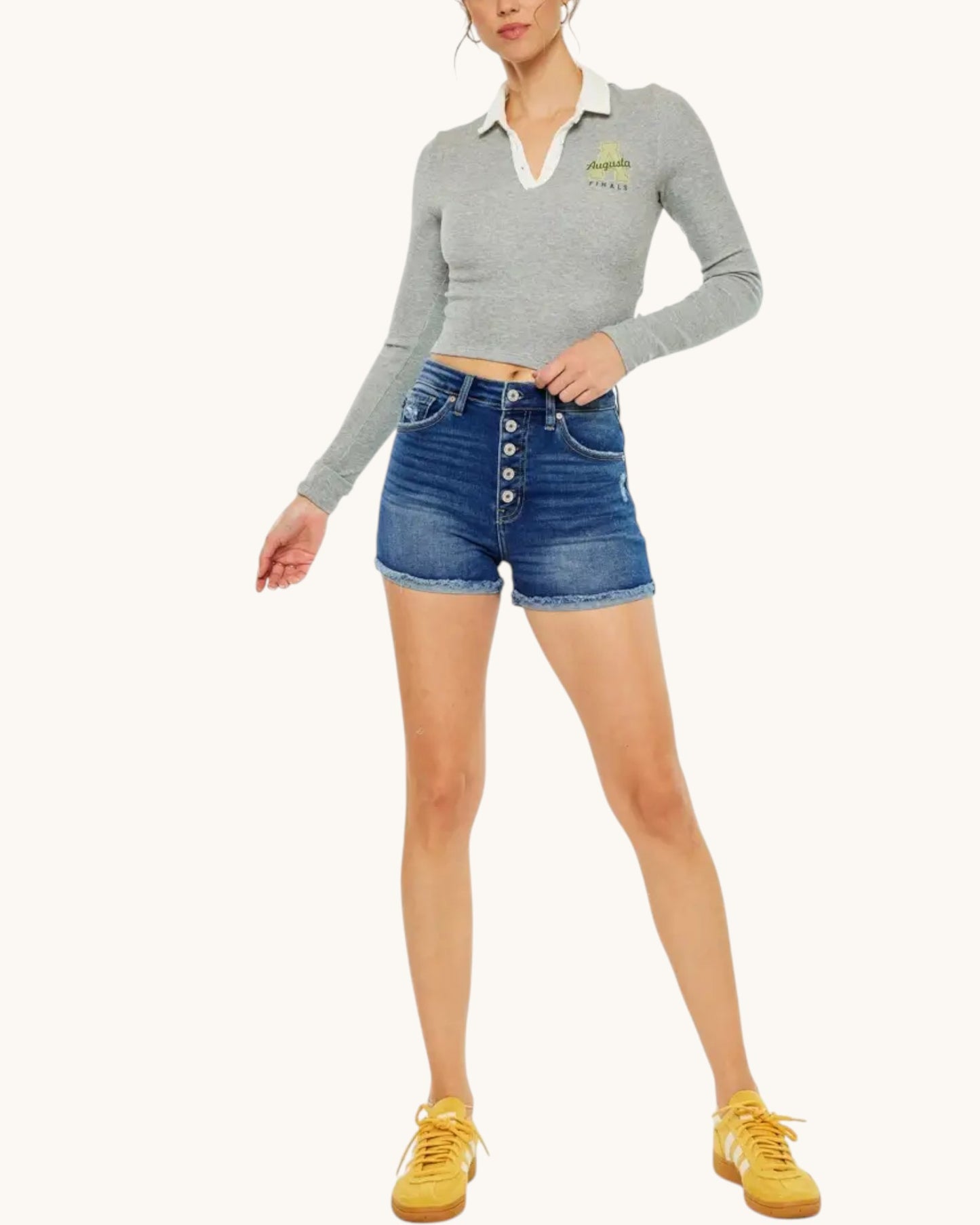 Person wearing a gray long-sleeve top with a logo, blue denim shorts, and yellow sneakers on a white background.