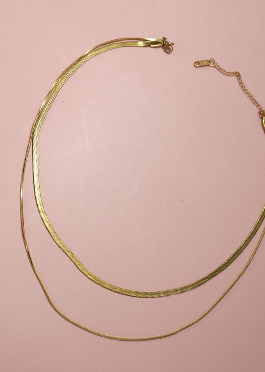 Gold n2-Layer Herringbone necklace on a pink background.