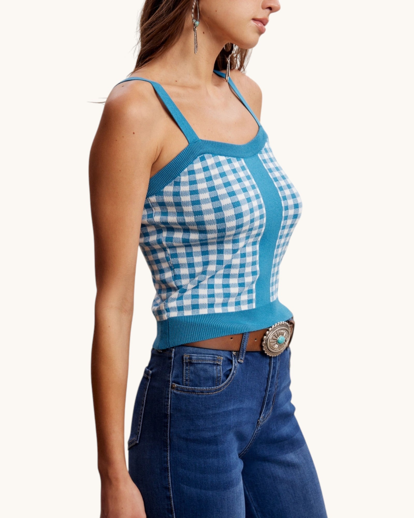 Woman wearing a blue and white checkered top with a turquoise border and blue jeans.