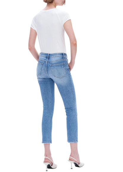 Woman wearing cropped blue jeans and a white top on a white background.