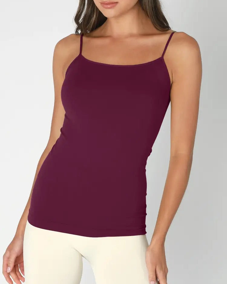 Woman wearing a purple/fig tank top and white pants on a gray background.