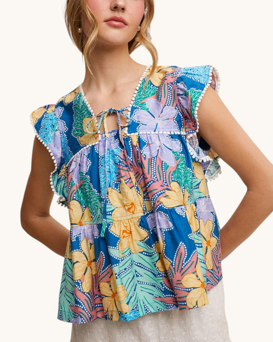 Woman wearing a colorful, tropical floral top with ruffled sleeves on a white background.