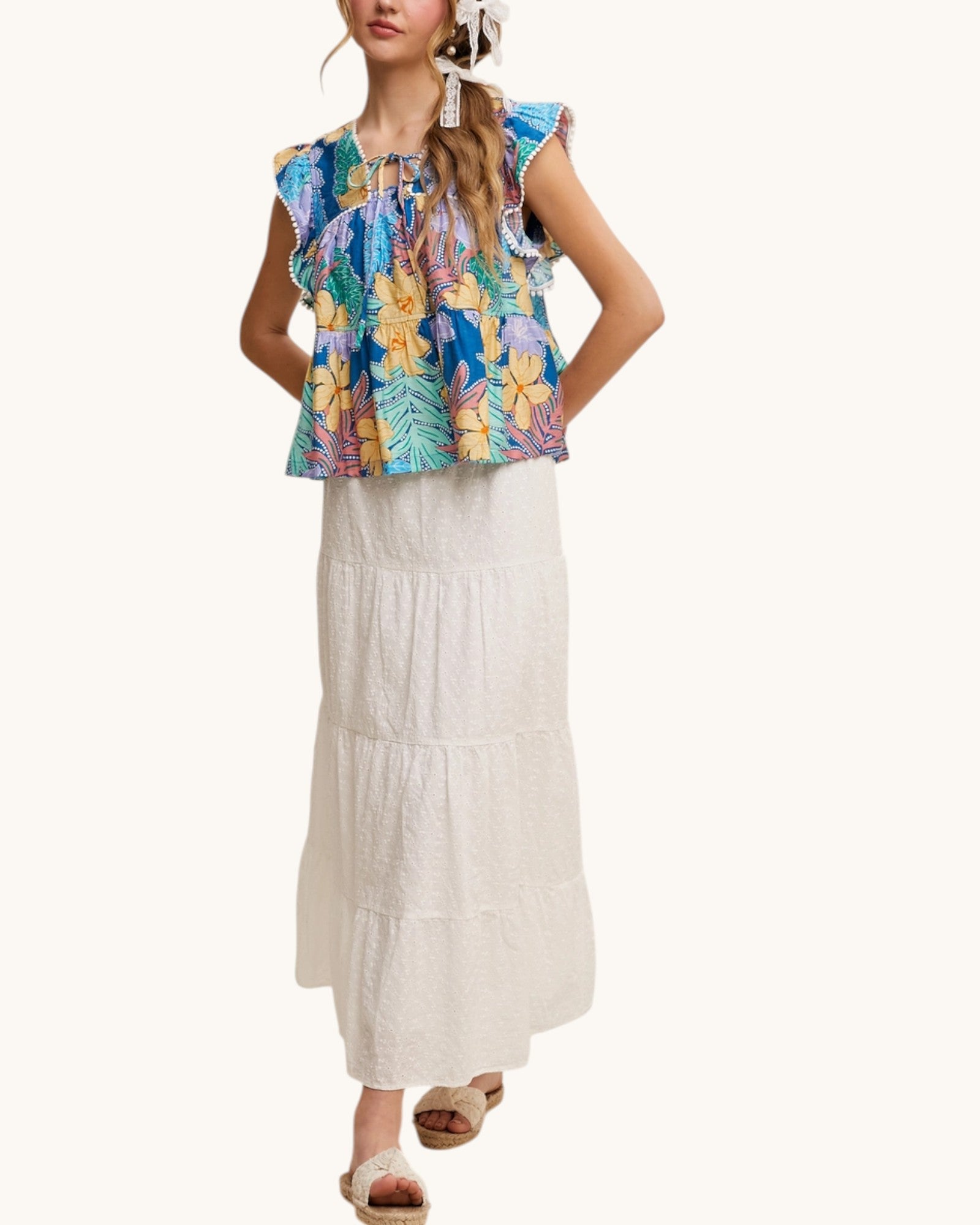 Woman wearing a colorful floral top and white skirt on a white background.