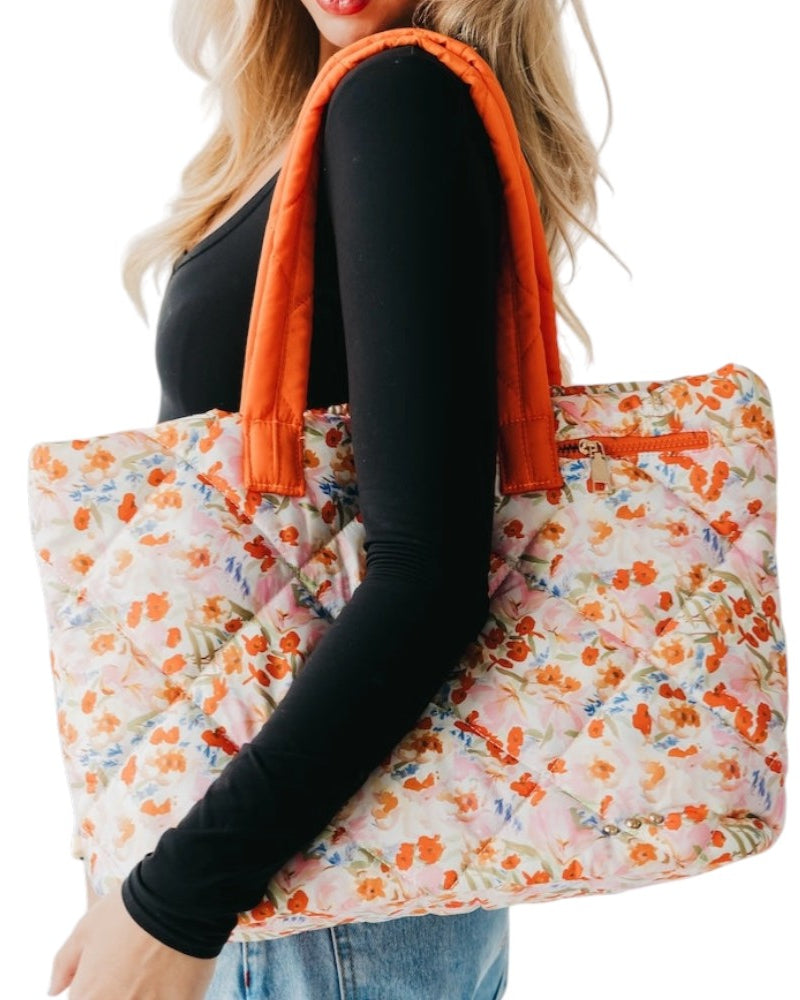 Person holding a floral tote bag with orange accents on a white background.