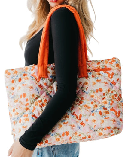 Person holding a floral tote bag with orange accents on a white background.