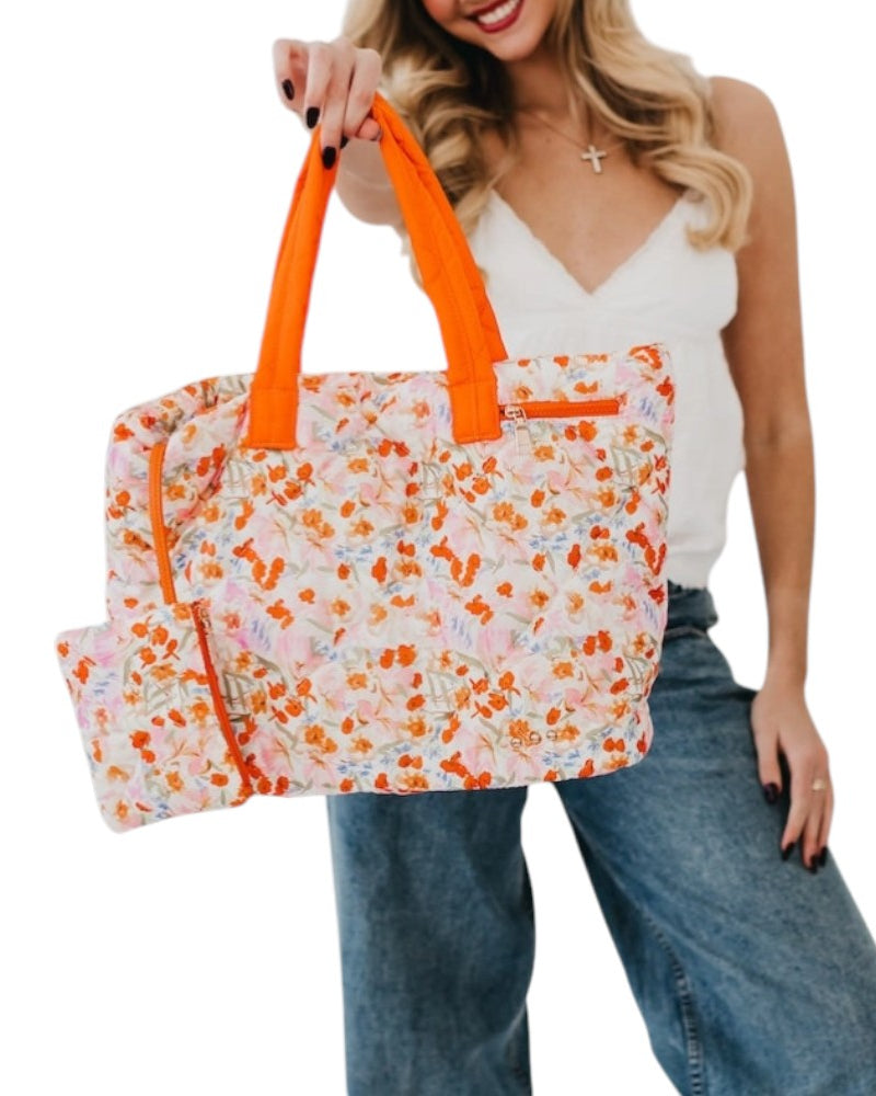 Woman holding a floral tote bag with orange handles on a white background.