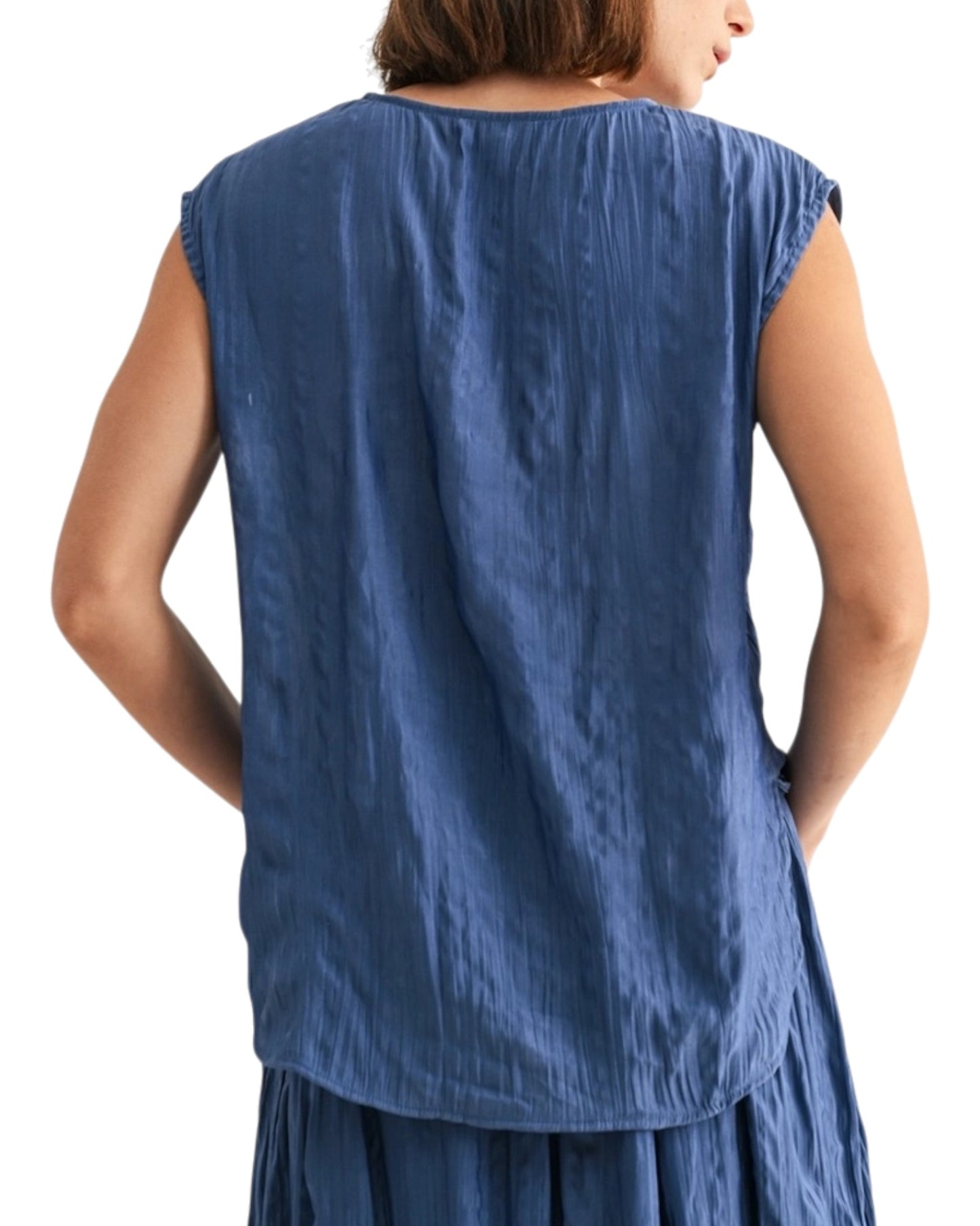 Woman wearing a blue textured sleeveless top on a white background.