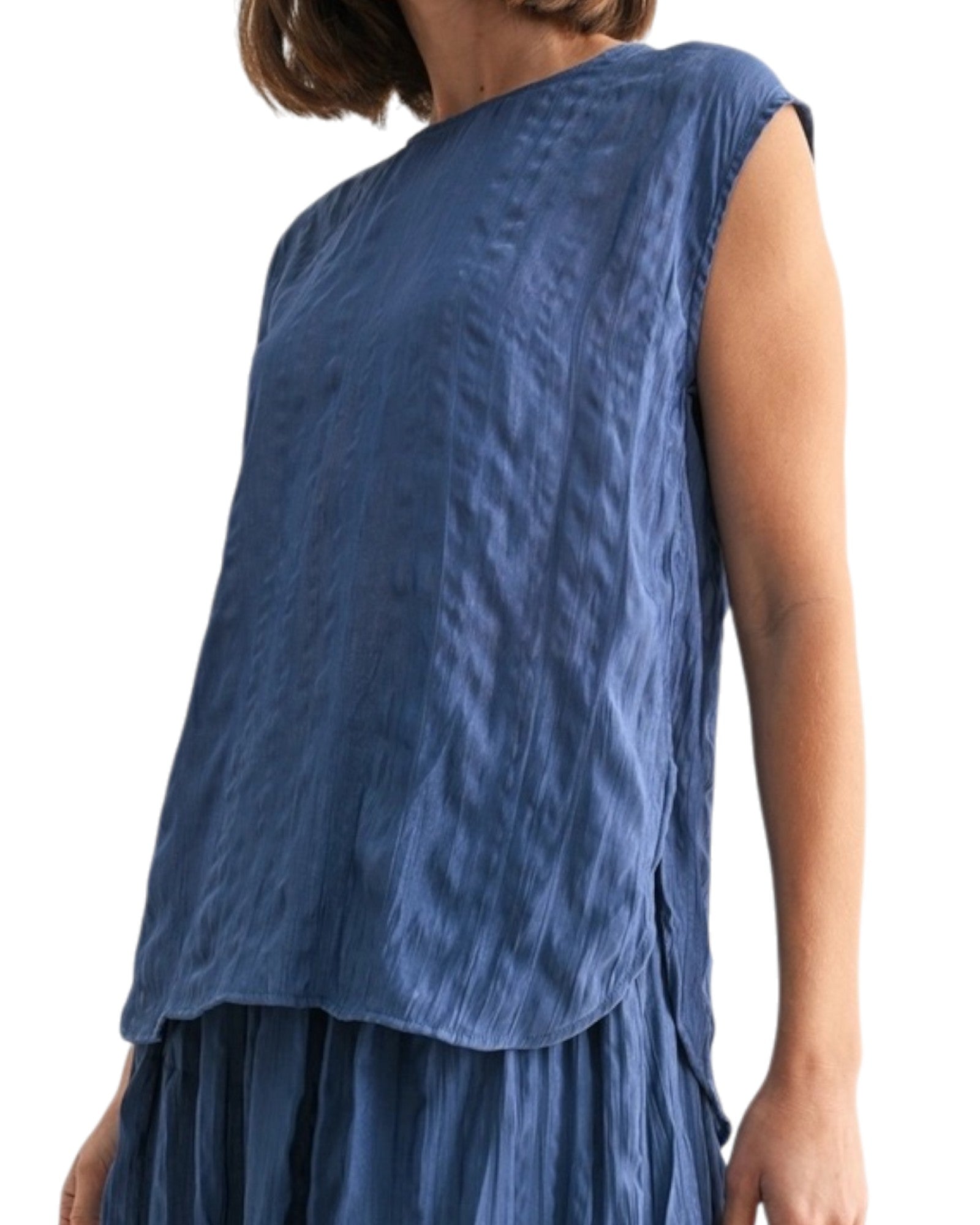 Woman wearing a blue textured sleeveless top on a white background.