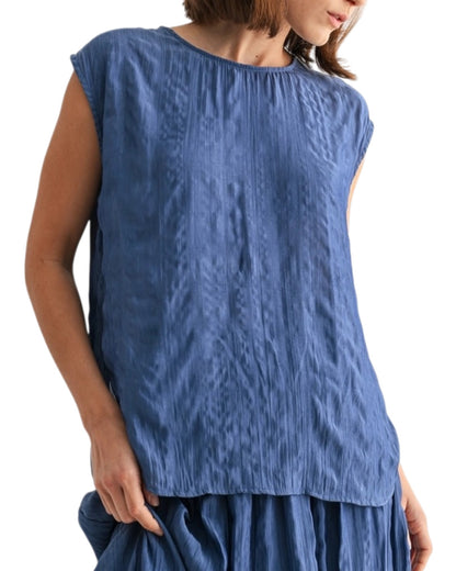 Woman wearing a blue textured sleeveless top on a white background.