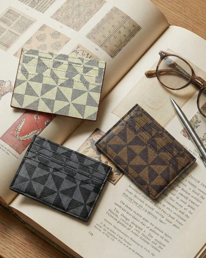 Three geometric-patterned card holders/wallets on an open book with glasses and a pen.