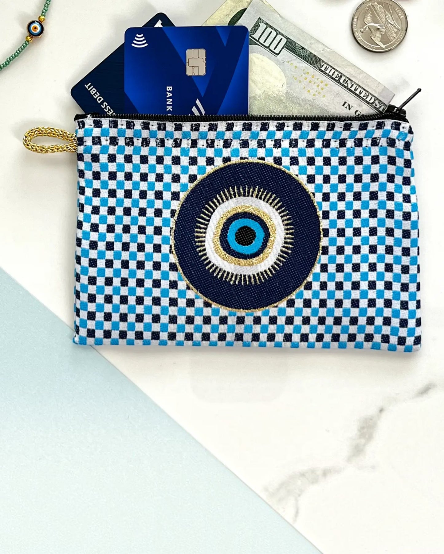 Checkered pouch with evil eye design containing money and cards on a marble surface.