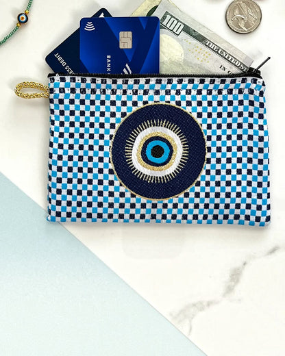 Checkered pouch with evil eye design containing money and cards on a marble surface.