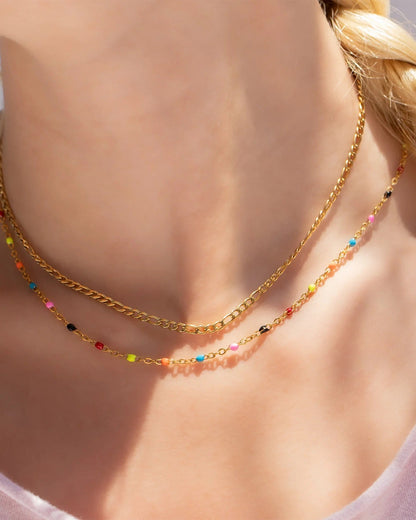 Gold necklace with colorful beads worn by a person with a blurred background.