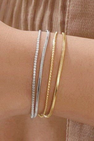 Two gold and one silver bracelet on a wrist against a brown background