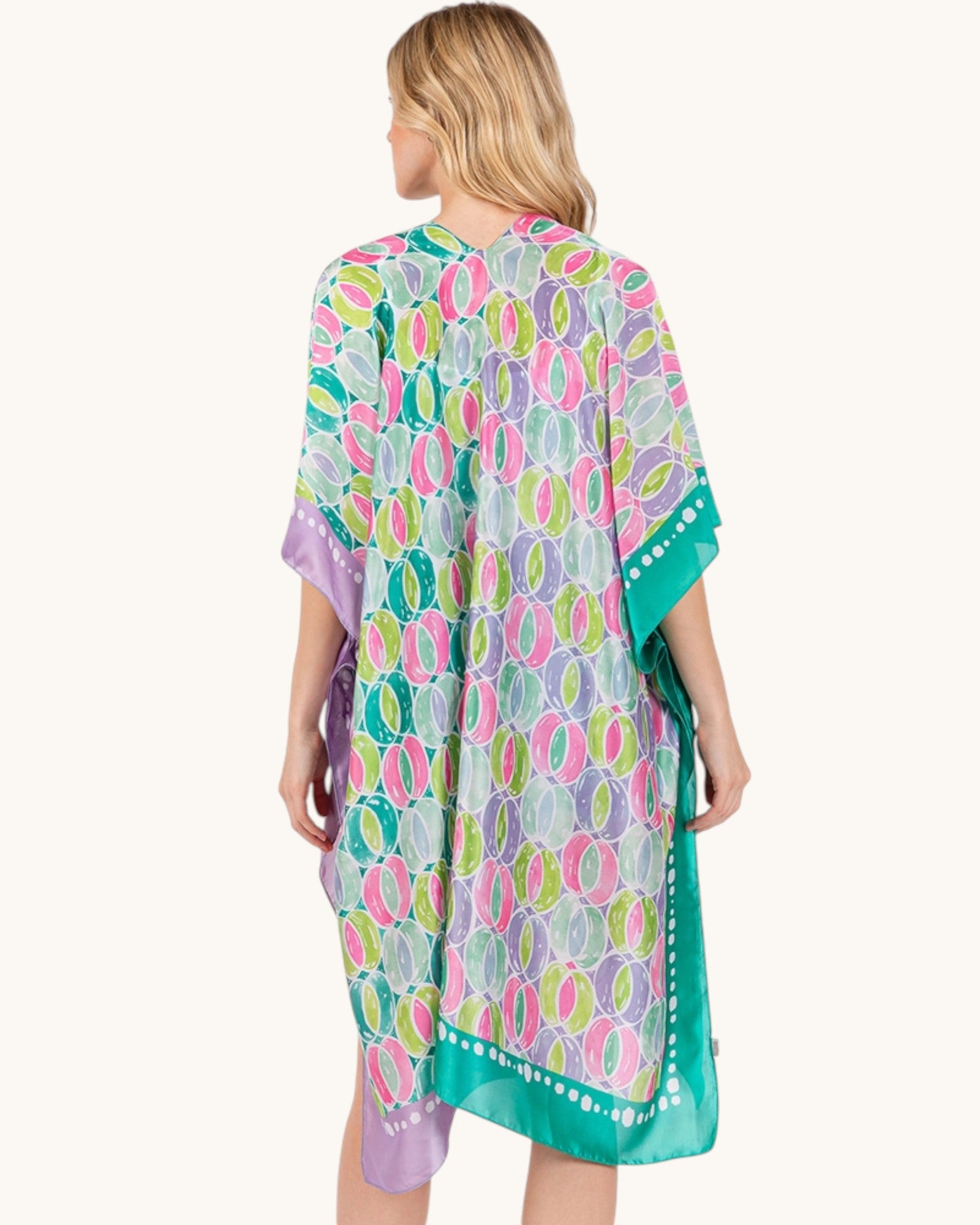 Back view of a woman wearing a green, purple and pink colorful patterned cover-up on a white background.