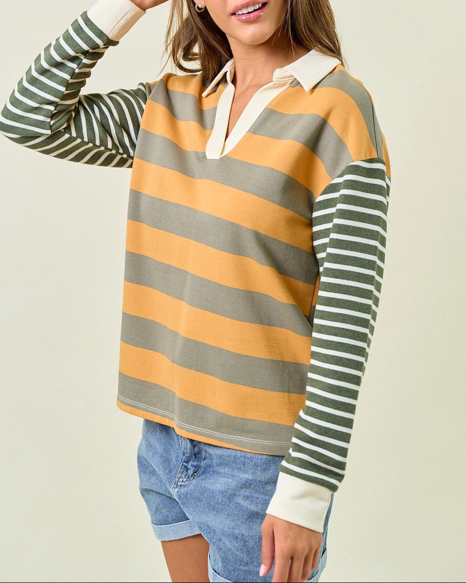 Woman wearing a muted green and mustard yellow striped rugby style shirt. 