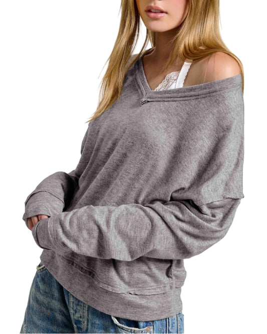 Woman wearing a gray oversized long sleeve top with raw edge trim on a white background.