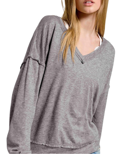 Woman wearing a gray oversized long sleeve top with raw edge trim on a white background.