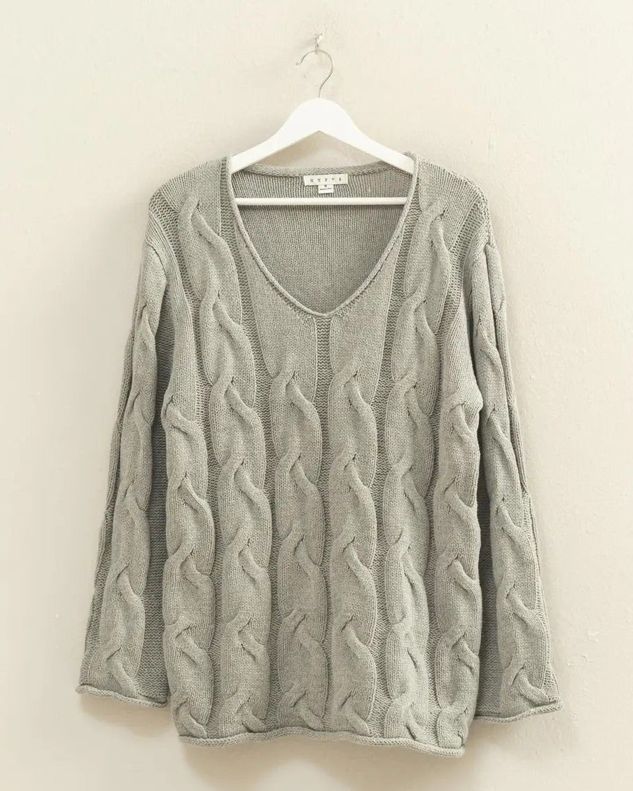 Gray cable knit sweater on a hanger against a beige wall.