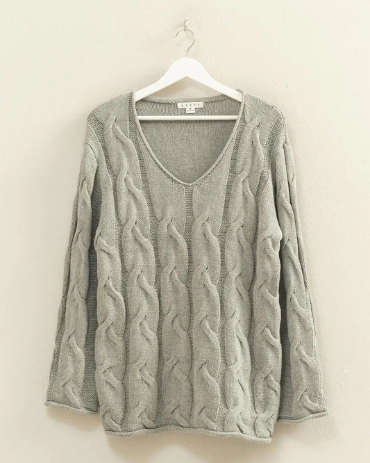 Gray cable knit sweater on a hanger against a beige wall.