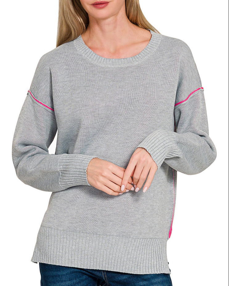 Woman wearing a gray sweater with pink contrast on a white background.