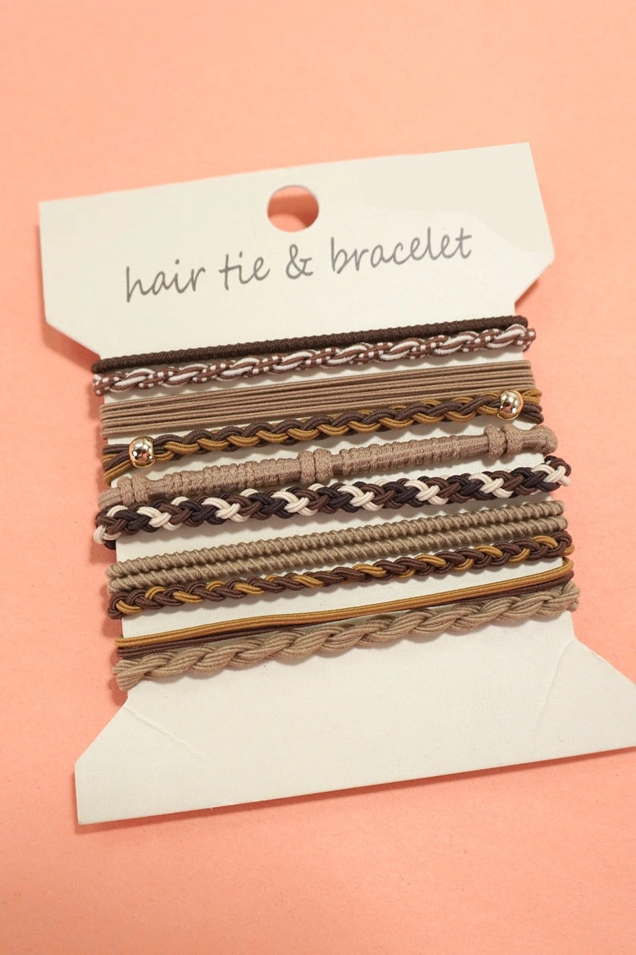 Set of hair ties and bracelets on a display card against a pink background