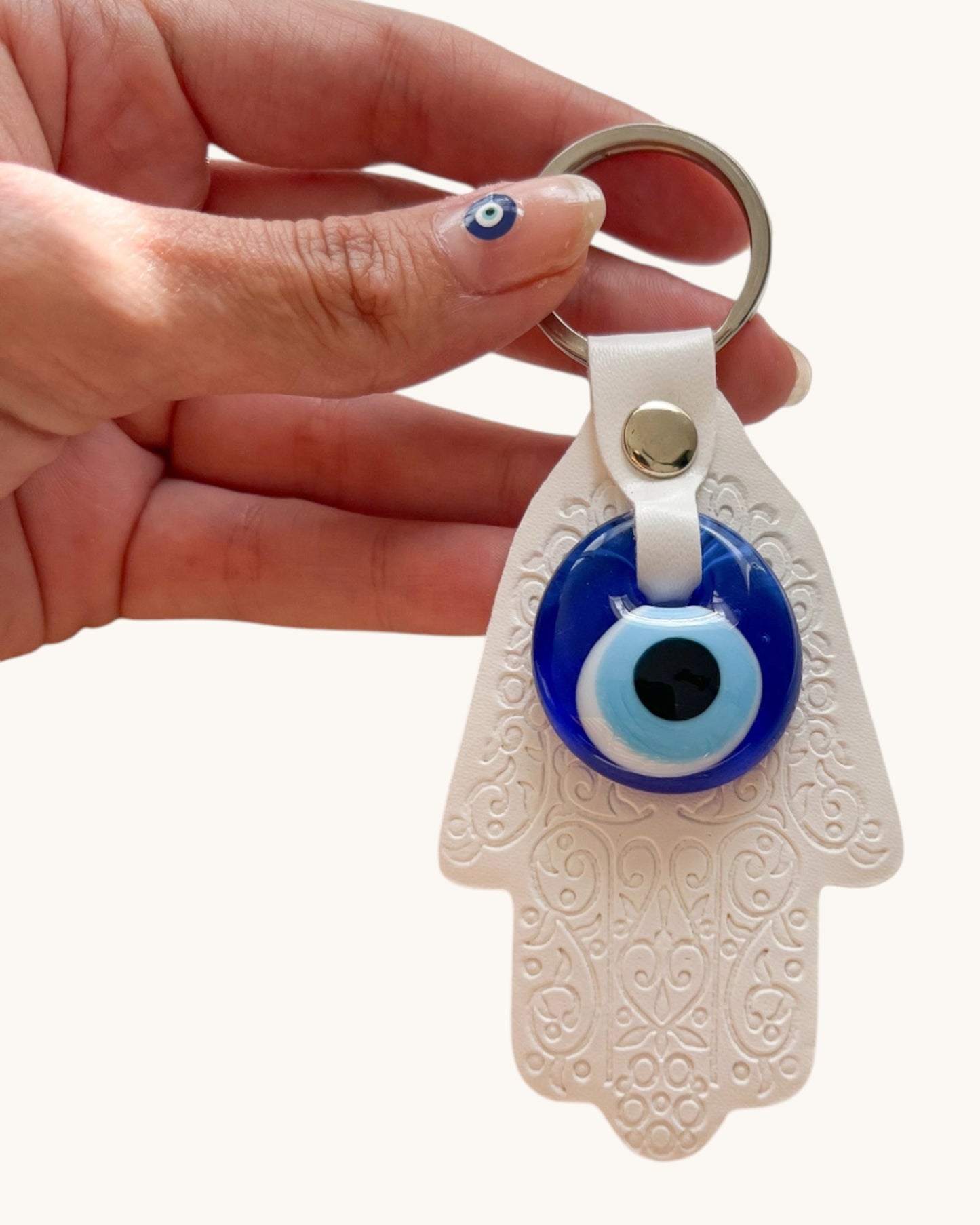 Hand holding a keychain with an eye design and white Hamsa hand.