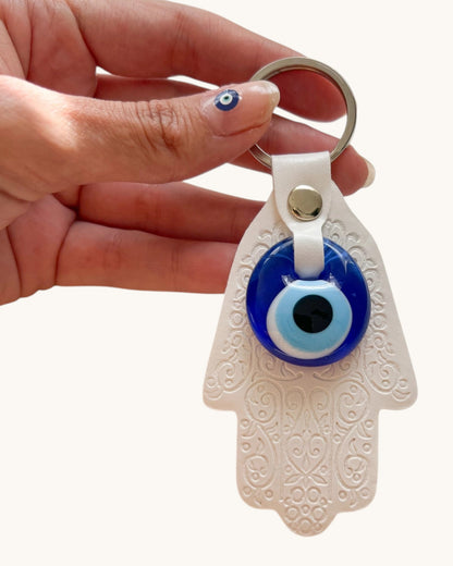 Hand holding a keychain with an eye design and white Hamsa hand.