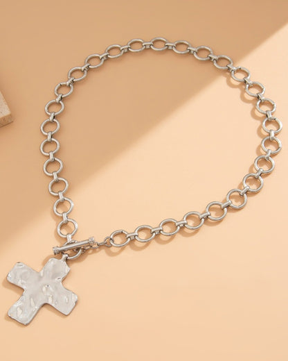 Silver chain necklace with a large cross pendant on a beige background.