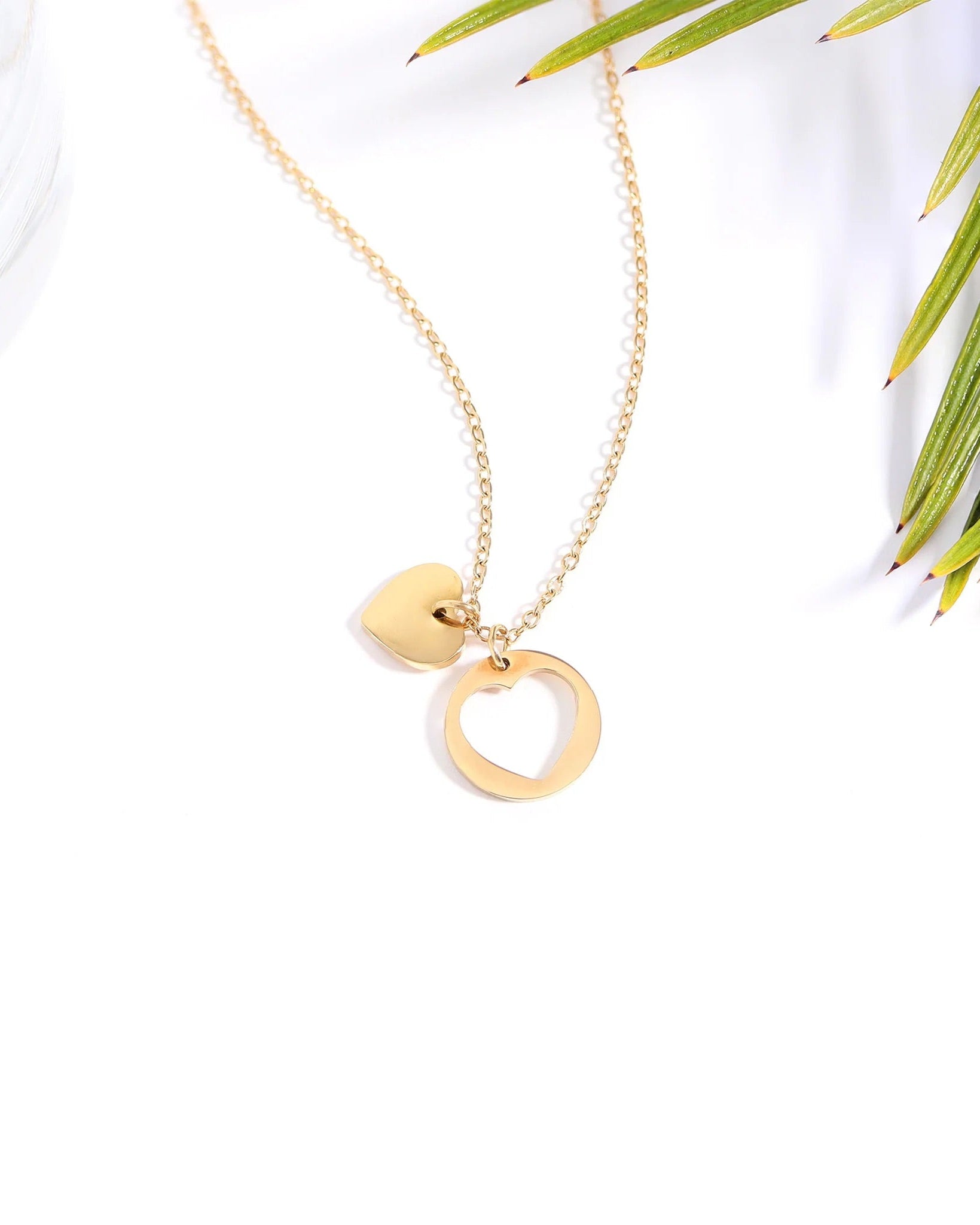 Gold necklace with heart-shaped pendants on a white background with green leaves.