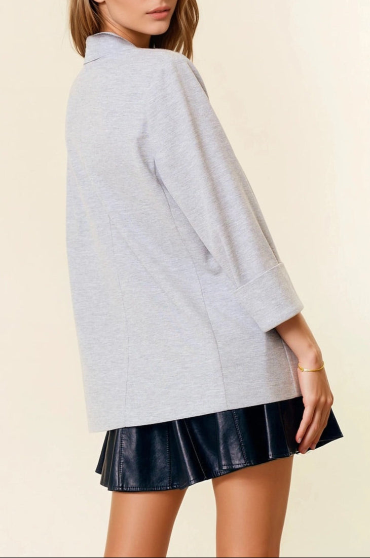 Woman wearing a light gray oversized sweater over a black pleated skirt on a beige background