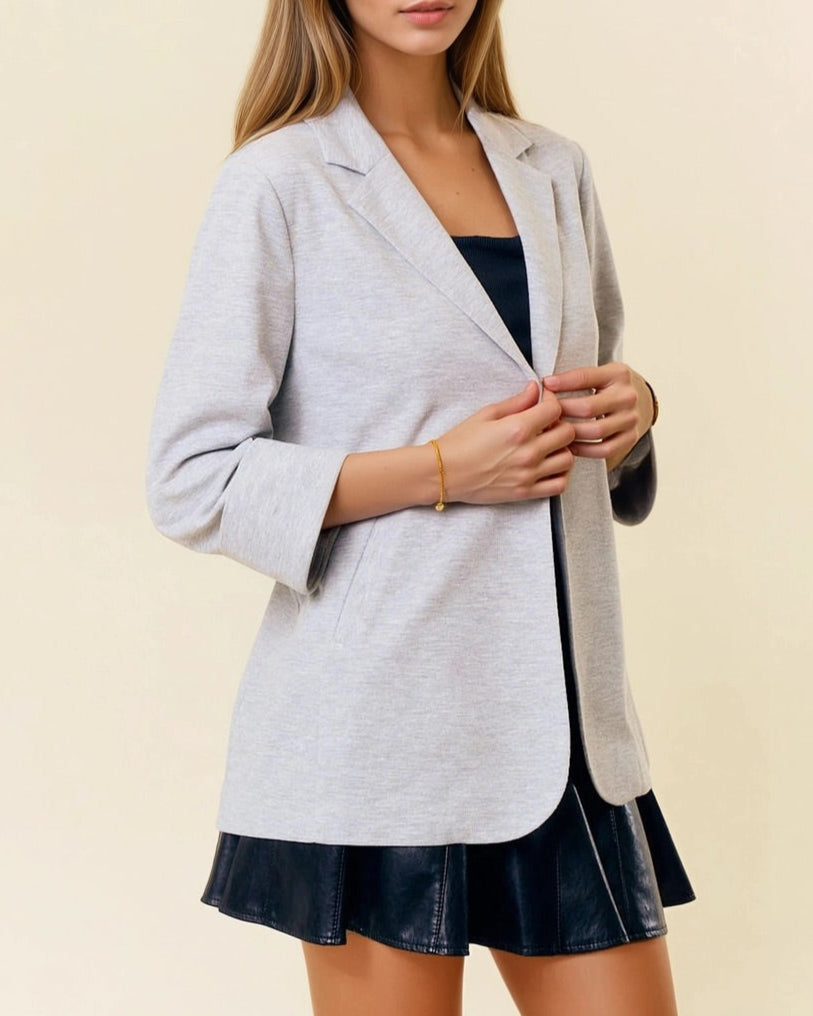 Woman wearing a light gray blazer over a black dress on a beige background.