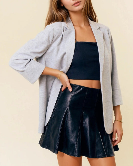 Woman wearing a gray blazer, black top, and black pleated skirt on a beige background