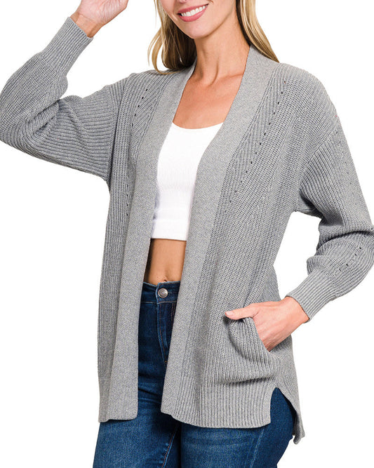 Woman wearing a gray eyelet cotton cardigan over a white top and blue jeans on a white background.