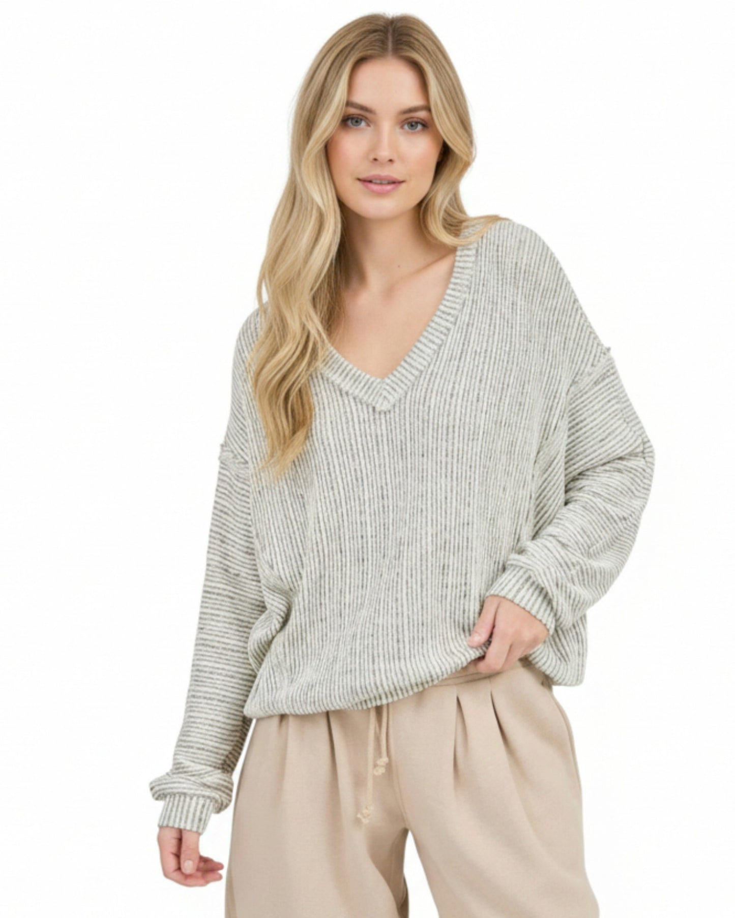 Woman wearing a light heathered oatmeal ribbed sweater and beige pants on a white background.