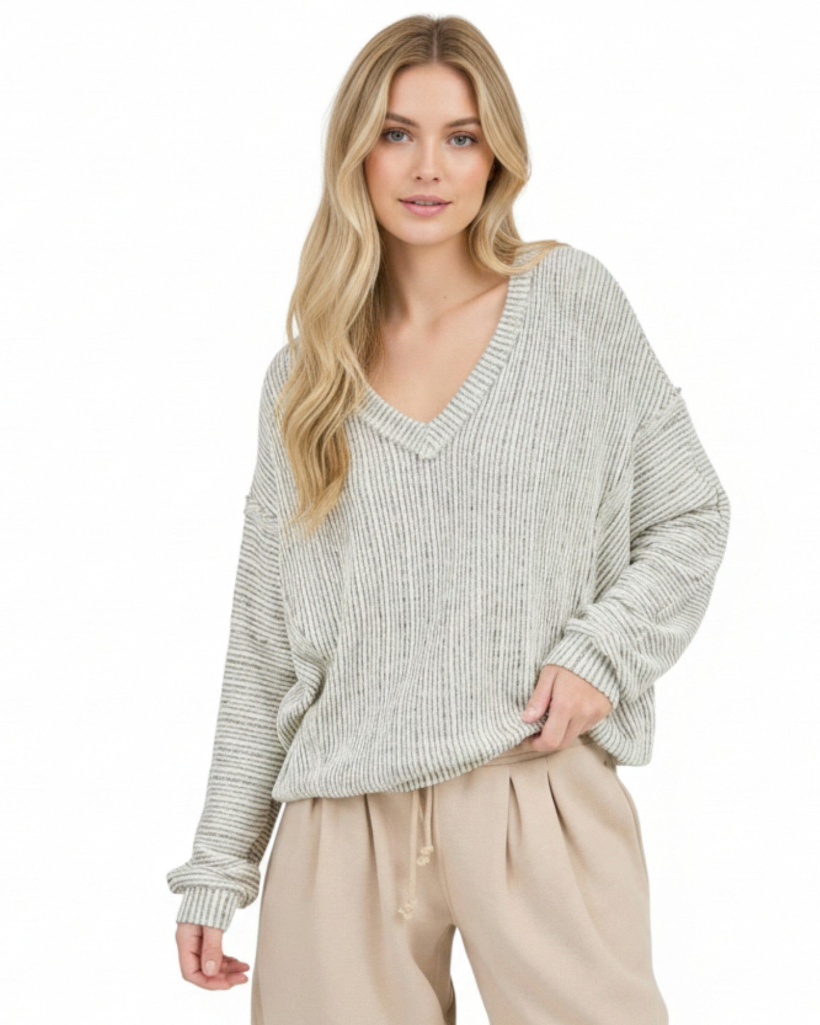 Woman wearing a light heathered oatmeal ribbed sweater and beige pants on a white background.