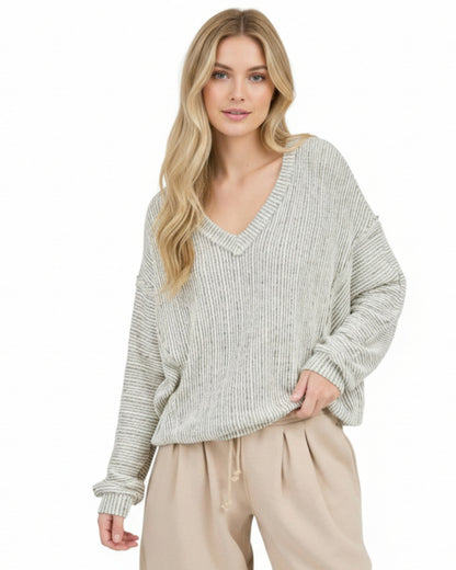 Woman wearing a light heathered oatmeal ribbed sweater and beige pants on a white background.