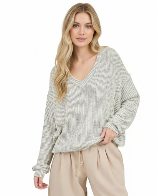Woman wearing a light heathered oatmeal ribbed sweater and beige pants on a white background.