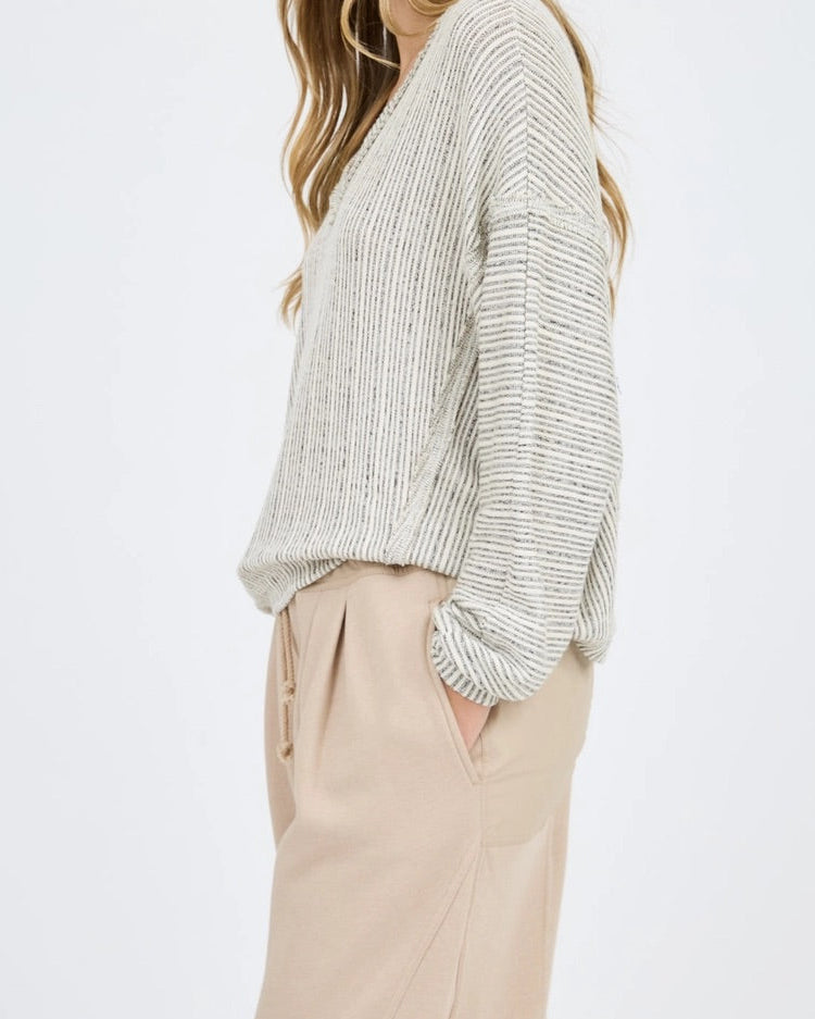 Woman wearing a light heathered oatmeal ribbed sweater and beige pants on a white background.