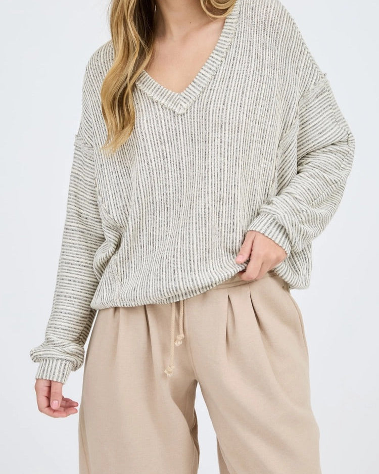 Woman wearing a loose-fitting, ribbed sweater and beige pants on a white background.