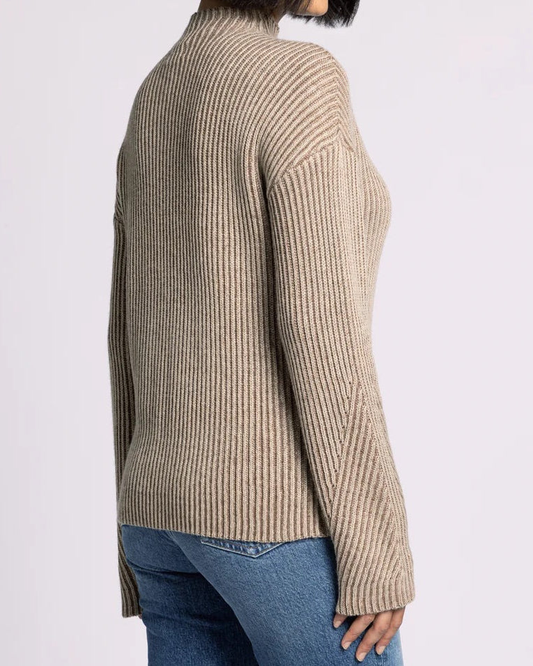 Woman wearing a beige ribbed sweater and blue jeans on a white background.