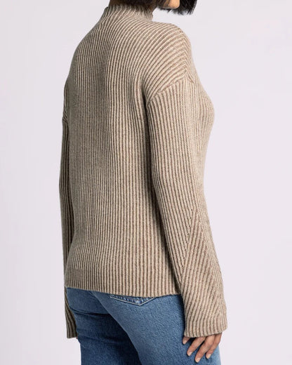 Woman wearing a beige ribbed sweater and blue jeans on a white background.