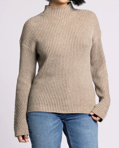 Woman wearing a beige ribbed sweater and blue jeans on a light gray background.