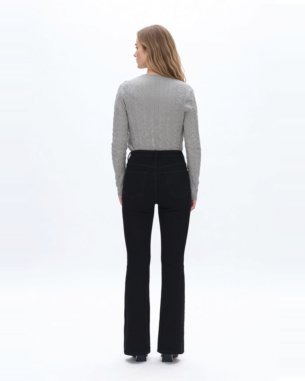 Back view of a woman wearing high rise flare denim black jeans with gray sweater.