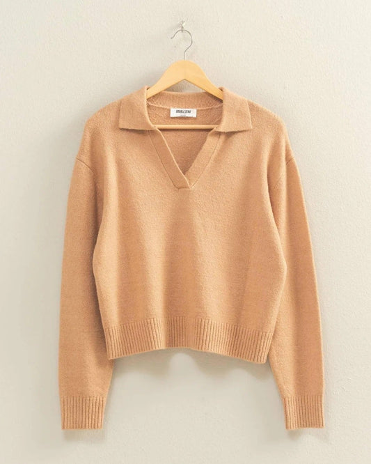 Tan sweater on a hanger against a beige wall.