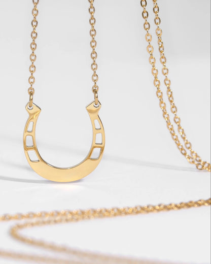 Gold horseshoe-shaped pendant on a gold chain against a white background.